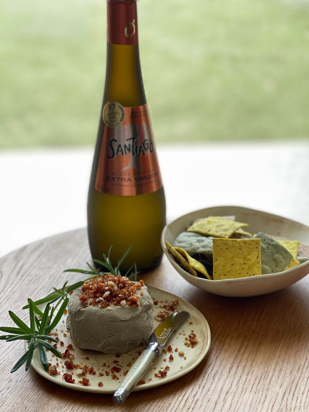 Plato con una porción de Paté con Almendras junto a bocaditos para untar y una botella de aceite de oliva Santiago Premium.