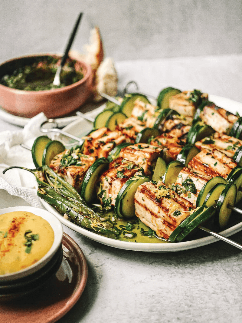 Plato que muestra cinco brochetas de albacora junto a dos recipientes de dips.
