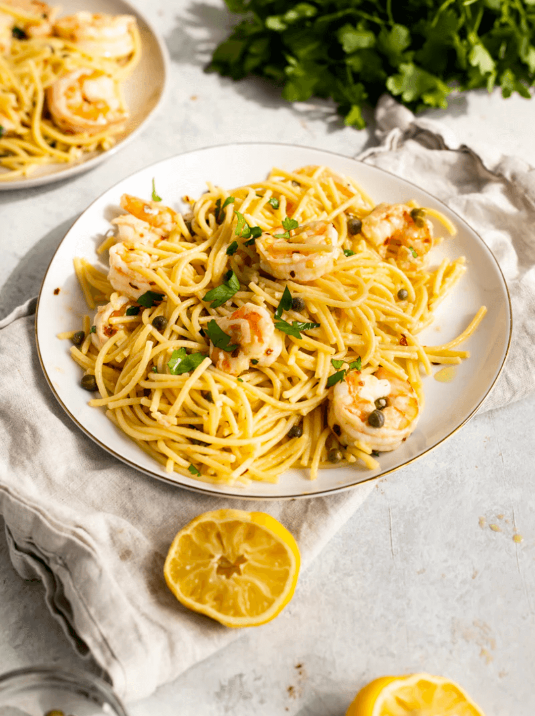 Pasta con camarones, alcaparras y limón servidos en un plato blanco y acompañado por una botella de aceite de oliva O-Live & Co