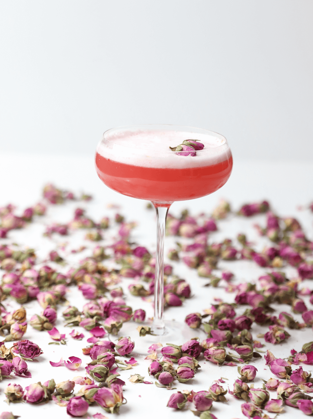 Cóctel de Rosas o Clover Cocktail sobre una mesa repleta de capullos de rosas.