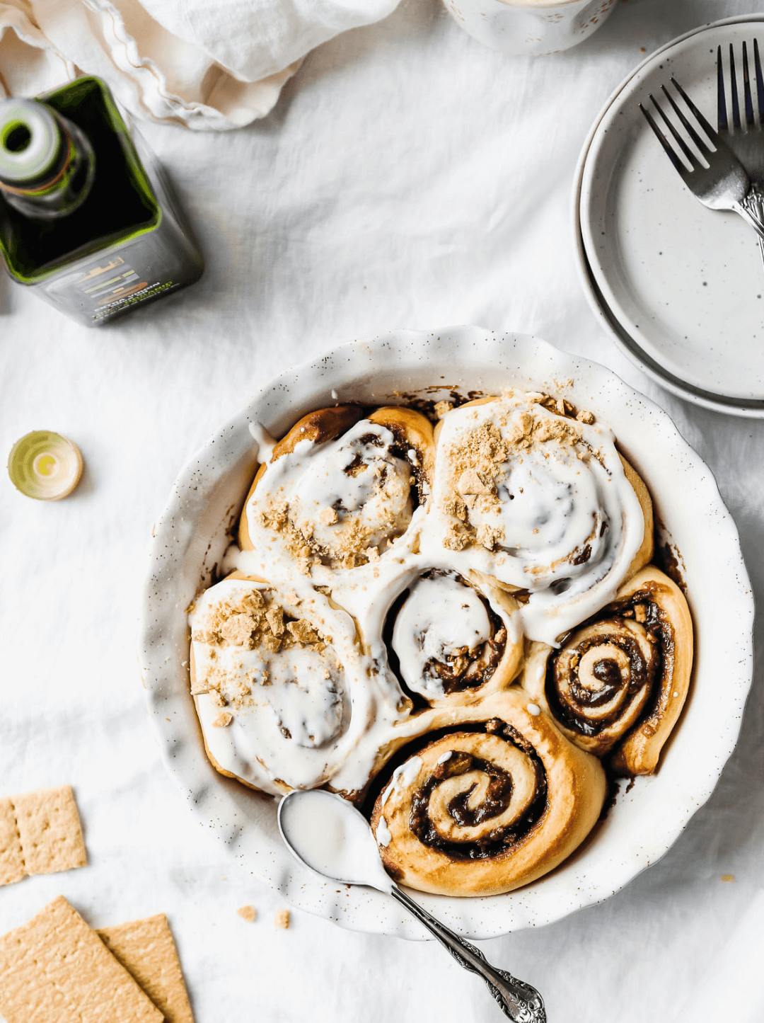 Recipiente blanco con Cinnamon rolls junto a una botella abierta de 500ml de aceite de oliva O-Live & Co.