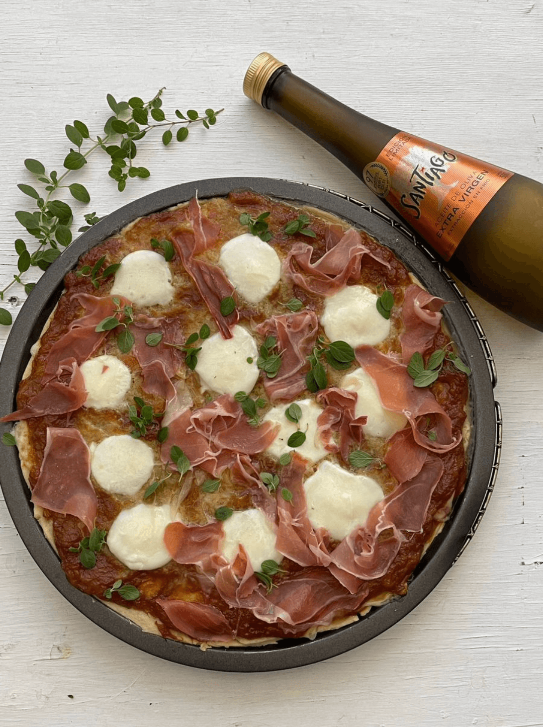 Pizza de cebolla caramelizada, mozzarella y jamón serrano siendo condimentada con aceite de oliva extra Virgen Santiago