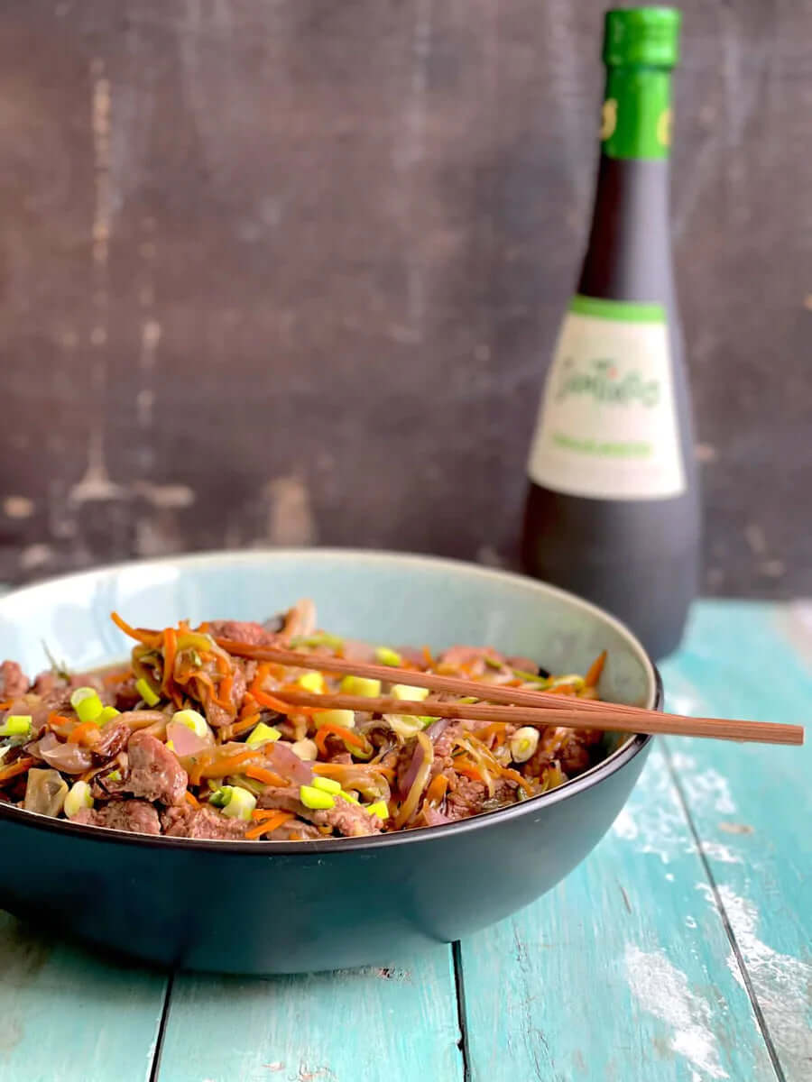 Carne salteadas con verduras servidas en un bowl acompañado con una botella de aceite de oliva Santiago Orgánico
