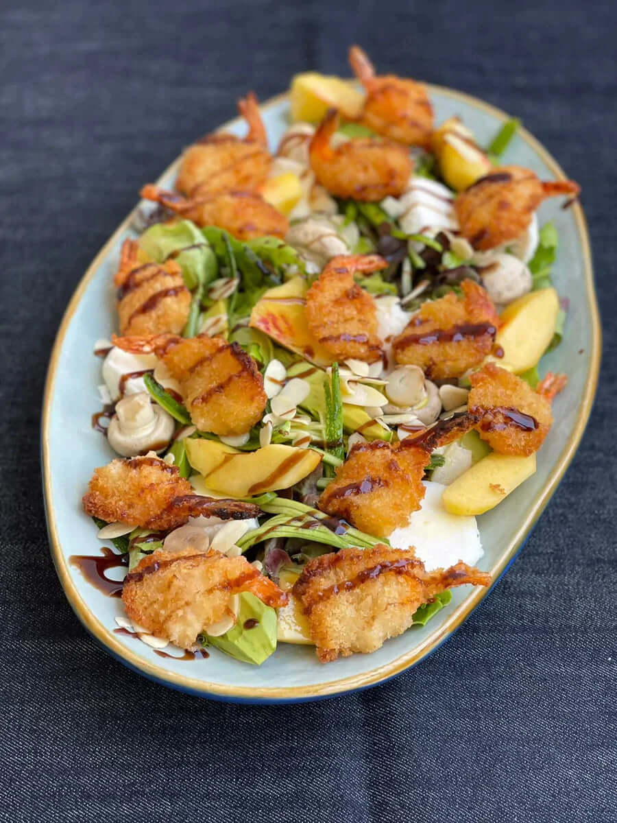 Recipiente con ensalada de camarones apanados con durazno y mozzarella.