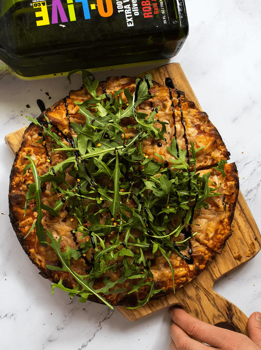 Pizza casera en una tabla de madera y una botella de aceite de oliva O-Live & Co