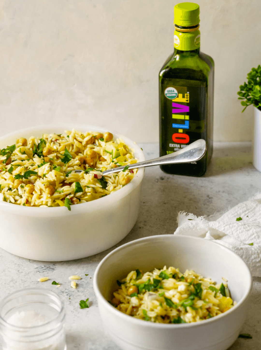 Dos recipientes blancos con ensalada mediterránea de limón y orzo junto a una botella de aceite de oliva O-Live & Co.
